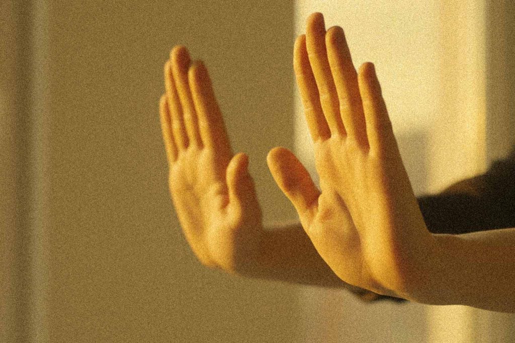Mãos fazendo um gesto suave de "parar", iluminadas por uma luz amarela, simbolizando o ato de dizer 'não' com gentileza e firmeza.