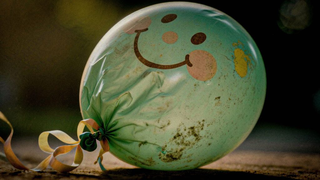 Balão murchando com um rosto sorridente no canto escuro de um quarto, representando a depressão infantil que muitas vezes é negligenciada ou mal interpretada.