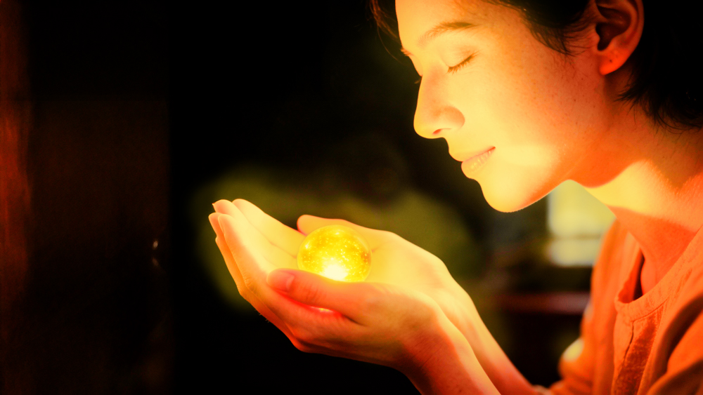 Mãos protegendo uma esfera de luz dourada, simbolizando o cuidado consigo mesmo e a autocompaixão durante tempos sombrios.