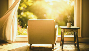 Uma poltrona de linho vazia diante de uma janela aberta para um jardim sereno, com o vapor de uma caneca subindo lentamente, representando o ócio criativo e o silêncio.