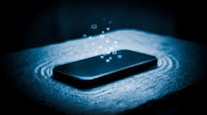 Telemóvel sobre uma mesa escura a vibrar suavemente enquanto bolhas de notificação brilhantes flutuam e desaparecem no ar, simbolizando a vacuidade e o frio das conexões digitais.